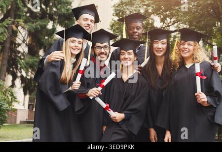 Laureati che hanno un abbraccio di gruppo vicino all'università Foto Stock