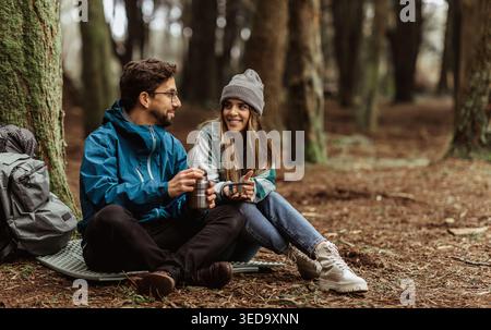 Felice giovane turista europeo ragazzo e donna in giacche con zaino riposo in campeggio foresta, godere di stagione fredda Foto Stock