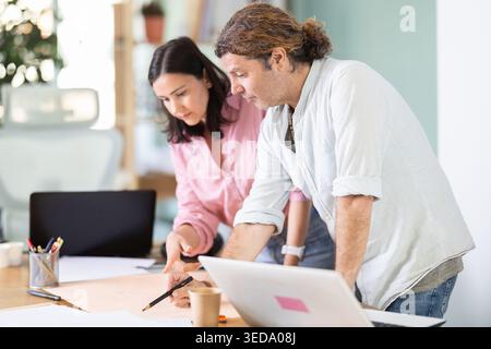 Colleghi di mezza età che discutono di un piano di costruzione appoggiati al tavolo dell'ufficio Foto Stock