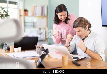 Colleghi di sesso maschile e femminile felici che si vantano di ottenere risultati di successo su un notebook Foto Stock