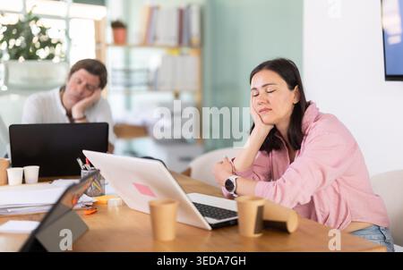 Donna di mezza età che dorme al tavolo dopo una lunga giornata di lavoro Foto Stock
