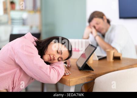 Donna di mezza età che dorme al tavolo dopo una lunga giornata di lavoro Foto Stock