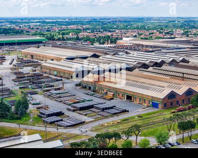 Veduta aerea della vasta acciaieria industriale con grandi magazzini e pile di tubi metallici sotto un cielo nuvoloso a Dalmine, Lombardia, Italia. Foto Stock