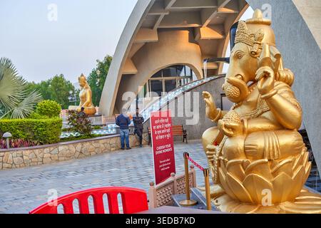 Statua dorata della divinità indù Ganesha seduto su un fiore di loto in primo piano, con una corona e ornamenti tradizionali intricati. Nel Foto Stock