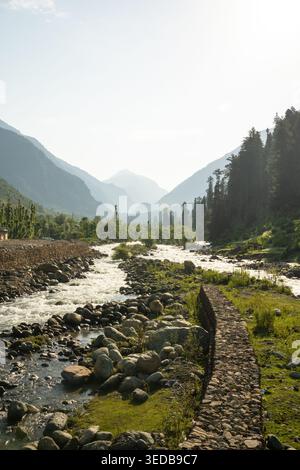 Tranquillo fiume che si snoda attraverso una valle verdeggiante con montagne nebbiose, ideale per viaggi, natura e promozioni avventurose a Pahalgam, Kashmir, India Foto Stock