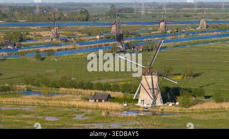 Vista aerea degli storici mulini a vento di Kinderdijk che si ergono lungo i canali blu nel lussureggiante paesaggio verde dei polder sotto la luce del sole a Kinderdijk, sud Foto Stock
