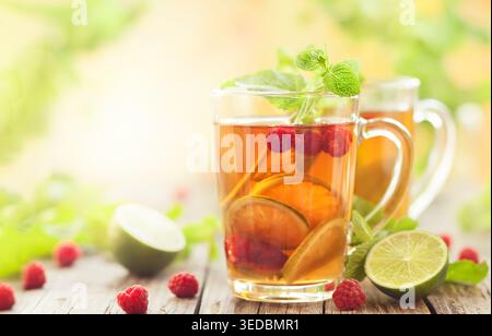 Bicchieri di tè estivo con lamponi, lime e menta su tavolo di legno Foto Stock