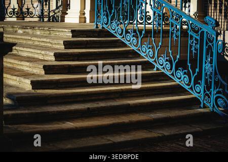 La luce del sole proietta lunghe ombre su gradini di pietra usurati, evidenziando i dettagli intricati di una ringhiera color ottanio decorata. La consistenza dei gradini intemprata Foto Stock