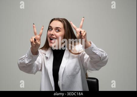 Giovane donna sorridente, che fa un segno di pace o di vittoria con entrambe le mani, celebrando il successo e la positività Foto Stock