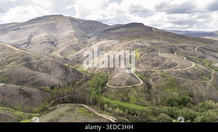 Vista aerea di tortuose strade sterrate che attraversano pendii di montagna bruciati e valli verdi sotto un cielo nuvoloso Provincia di Ourense, Spagna. Foto Stock
