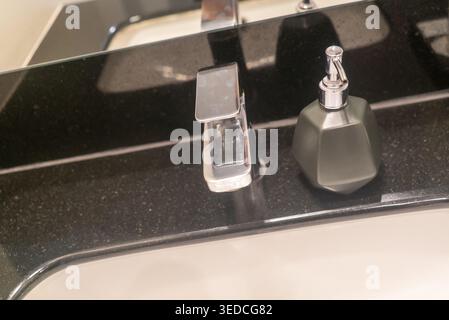 Un moderno lavandino da bagno con un elegante rubinetto e un elegante dispenser di sapone su un ripiano lucido, che mette in risalto la pulizia e il contemporaneo Foto Stock