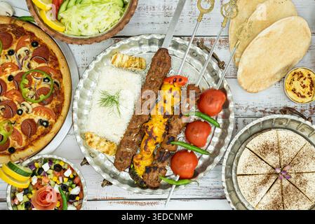 Deliziosi kebab di shish e pollo, pizza speciale al peperoni, contorni di insalate e salse e una cheesecake dolce Foto Stock