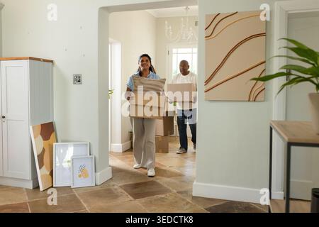 Coppia afroamericana che porta scatole mobili e cuscini a strisce mentre entra nel foyer piastrellato Foto Stock