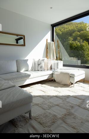 Il divano bianco componibile con chaise longue è esposto alla luce del sole presso una finestra con cornici nere e soffici getti Foto Stock