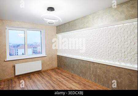 Camera moderna e vuota con pannelli decorativi retroilluminati a parete, pavimento in legno e radiatore a finestra. Interni eleganti, design contemporaneo e concetto di ristrutturazione Foto Stock