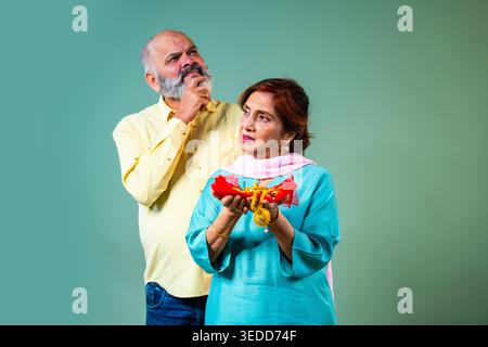 Una coppia anziana asiatica anziana in pensione preoccupata che tiene insieme gioielli d'oro mentre pensa profondamente a cosa fare riguardo a te Foto Stock