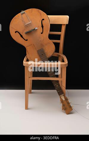Chitarra acustica vecchia e rotta capovolta su una sedia vecchia e rotta. Fotografato su sfondo bianco e nero. Foto Stock
