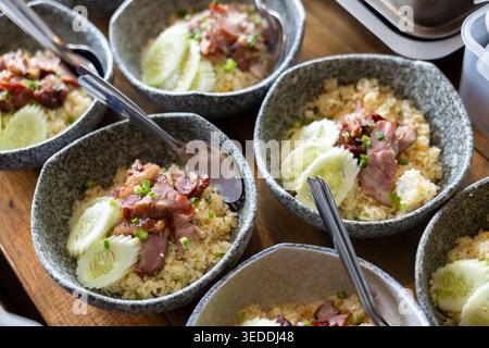 Delizioso riso fritto salato ricoperto di maiale arrosto e cetriolo fresco a fette servito in ciotole di ceramica rustica pronto per un appetitoso e appetitoso Foto Stock