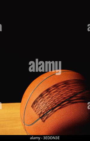 Pallacanestro arancione con l'ombra della rete da basket e del canestro su sfondo nero. Foto Stock