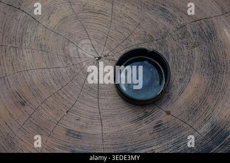 Primo piano di un ceppo di legno con posacenere contenente liquido iridescente. Foto Stock