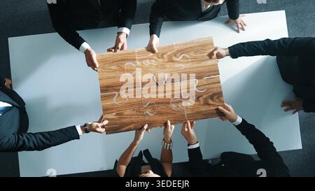 Uomini d'affari qualificati che mettono insieme il puzzle al tavolo delle riunioni. Un gruppo di team aziendali eterogenei e intelligenti collega o risolve i problemi insieme. Squadra Foto Stock