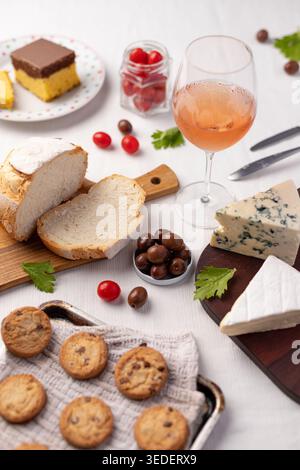 Su un tavolo ci sono fette di pane, diversi tipi di formaggio, biscotti, una bevanda e piccoli pomodori. Questa scena mostra un incontro di cibo con vari Foto Stock