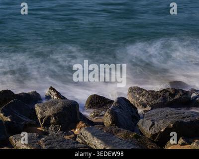 Onde oceaniche che si innalzano sulle rocce costiere con un effetto di lunga esposizione Foto Stock