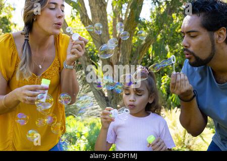 Diverse famiglie che soffiano bolle con bottiglie con tappo al neon e bacchette nel parco soleggiato con mustard-top Foto Stock