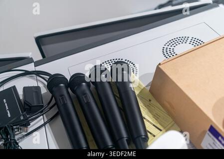 Una collezione di microfoni neri disposti su una superficie bianca, circondati da apparecchiature audio e cavi, perfetti per la registrazione del suono e la performa dal vivo Foto Stock