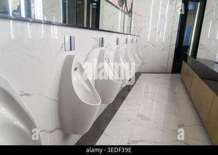 Un bagno elegante e moderno con una fila di orinatoi bianchi contro un'elegante parete in marmo, che sfoggia un design contemporaneo e pulizia in bagno Foto Stock