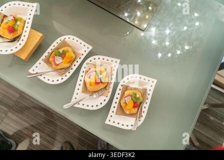 Trio di mini dessert con coloratissimi condimenti di frutta serviti su eleganti piatti bianchi. Perfette per feste, eventi o mostre culinarie, queste specialità bri Foto Stock