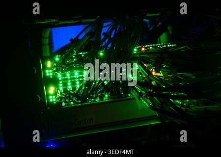 Immagine ravvicinata di uno switch di rete illuminato con numerosi cavi. Le luci verdi lampeggianti indicano i collegamenti attivi e la comunicazione digitale Foto Stock
