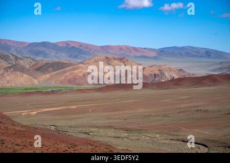 Ampia vista della catena montuosa dell'Altai nella Mongolia occidentale. L'immagine mostra pendii di montagna aridi con distinti strati sedimentari e terreno rossastro dentro Foto Stock