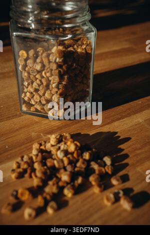 Vaso in vetro di pane con granuli versati su un tavolo. Prodotto naturale per l'apicoltura, ricco di vitamine, superfood biologico e concetto di nutrizione sana Foto Stock