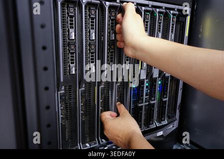Una vista ravvicinata delle mani che gestiscono un server dati in un rack server, che mostra gli intricati componenti e le luci della tecnologia moderna in un centro dati Foto Stock