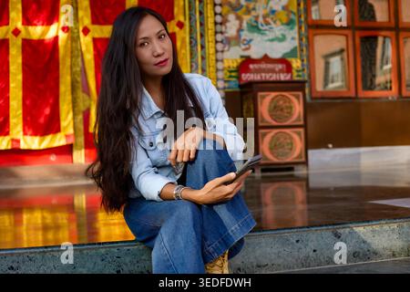 Ragazza asiatica seduta sul pavimento del tempio con lo smartphone in mano Foto Stock