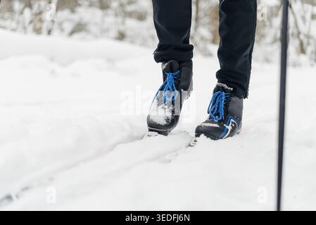Gambe da vicino e stivali alpini blu nero con lacci blu e logo bianco in neve soffice e profonda. Stazione sciistica con alberi e seggiovia sullo sfondo. Sci alpino in località invernale per le vacanze in montagna Foto Stock