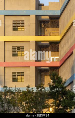 Vista di una facciata moderna di un edificio caratterizzato da colorate bande orizzontali e rete di sicurezza dietro alberi verdi nella città di Taipei, Taiwan. Foto Stock