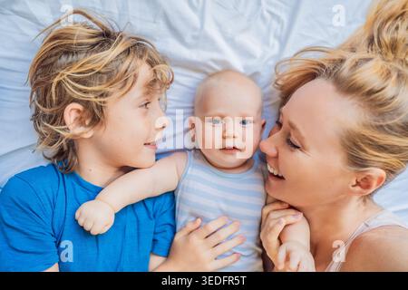 Madre sdraiata sul letto con due figli, neonato e bambino più grande a casa. La famiglia ama trascorrere del tempo insieme, legandosi e rilassandosi. Maternità Foto Stock