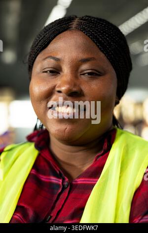 Ritratto di una donna nera con giubbotto di sicurezza che lavora in magazzino, manodopera a supporto della movimentazione dei pacchi e della logistica delle spedizioni. Trasporto e-commerce nel centro di distribuzione. Foto Stock