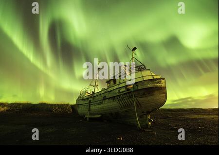 Vista di una vecchia barca da pesca in legno sotto la vibrante aurora boreale verde che danzerà attraverso il cielo stellato di Olafsvik, Snaefellsbaer, Icela Foto Stock