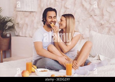 La coppia gode della colazione insieme in un accogliente ambiente interno con spuntini e bevande Foto Stock