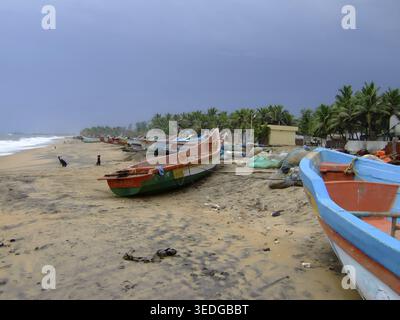 Barche da pesca su una spiaggia sotto un cielo nuvoloso fiancheggiato da palme, Mamallapuram, India Foto Stock