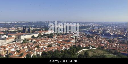 Vista panoramica di Praga, ampia vista della città verso il castello di Praga, Hradcany, la cattedrale di San Vito, Moldava, vigneti, dietro foreste e cieli blu Foto Stock