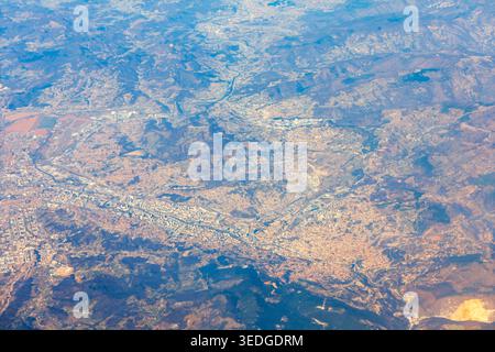 La vista aerea cattura una città estesa tra colline ondulate e montagne dall'alta quota. Il paesaggio urbano si estende attraverso valli con strade visibili Foto Stock