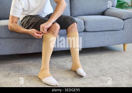 Uomo che indossa calzini a compressione beige per il supporto venoso varicoso a domicilio Foto Stock
