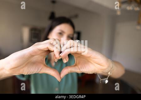 Donna che forma un gesto cardiaco con le mani al chiuso Foto Stock