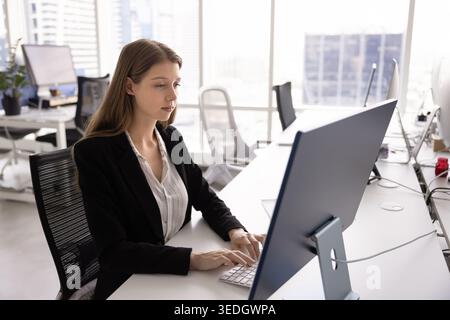 Donna seria che digita sulla tastiera mentre guarda un monitor di grandi dimensioni Foto Stock