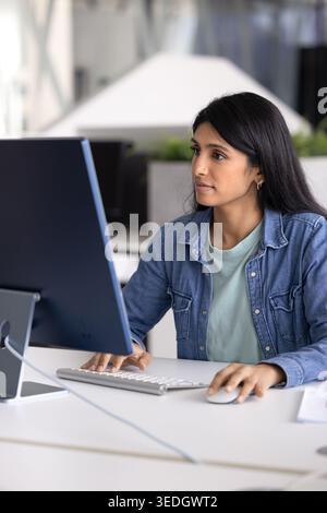 Giovane donna indiana che analizza i rapporti, lavora alla presentazione usando il PC Foto Stock