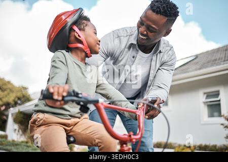 Sorridi, famiglia nera e bambino con bicicletta all'aperto per l'apprendimento, il supporto dei genitori e il legame. Felice, padre e bambino che aiuta con la bici come guida Foto Stock